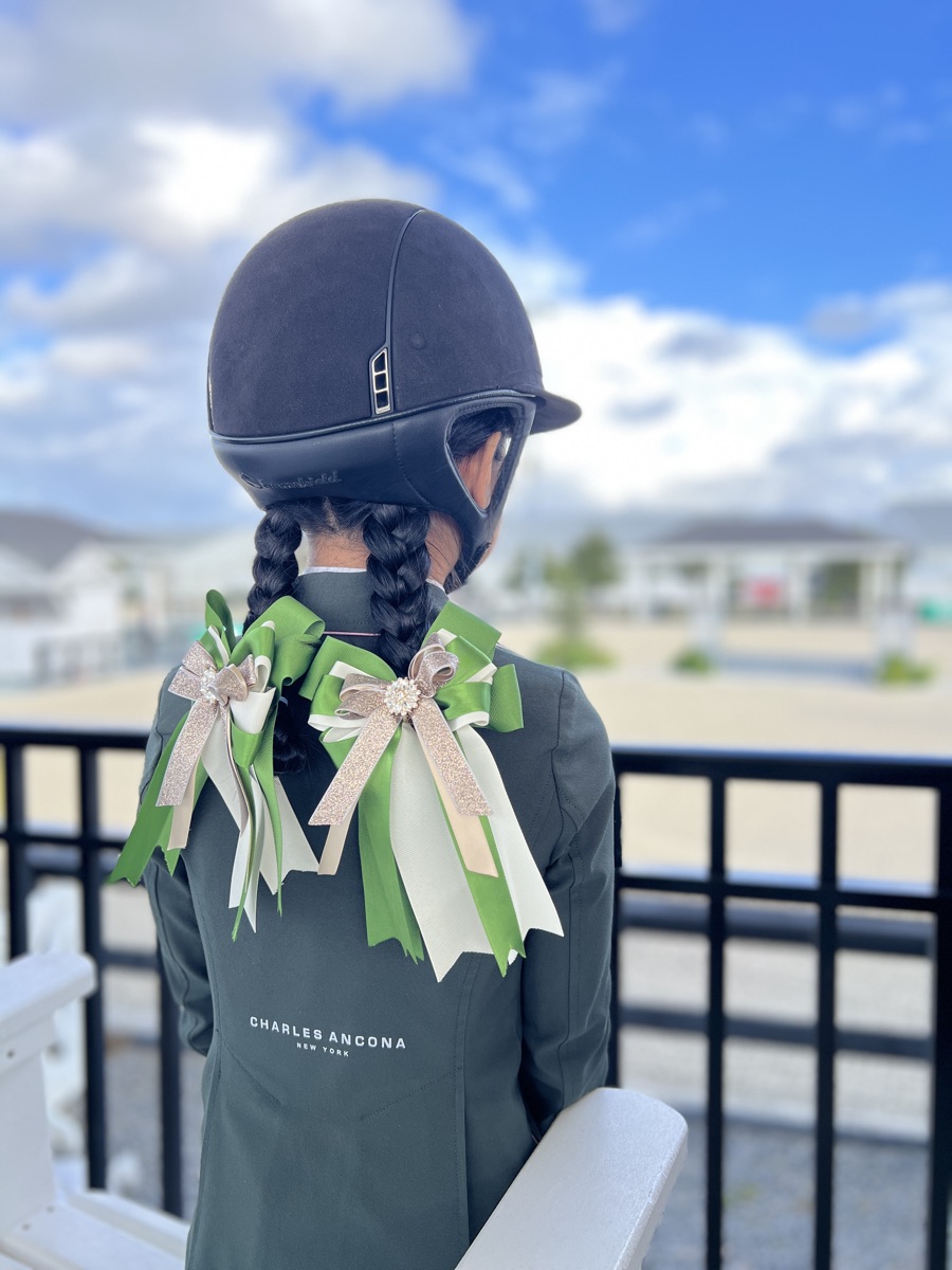 A young hunter rider in a Charles Ancona jacket wearing custom green and champagne bows in her braids
